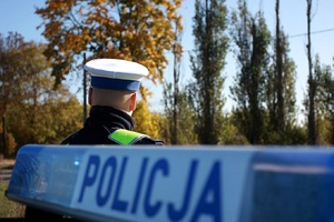 Policjant stoi przed radiowozem.