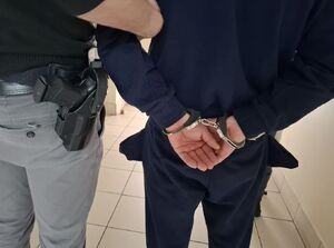 Policjant prowadzi osobę zatrzymaną.