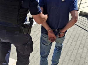 Policjanci prowadzą zatrzymanego do radiowozu.