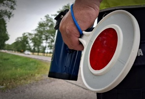 Policjant trzyma tarczkę do zatrzymywania pojazdów i miernik prędkości.