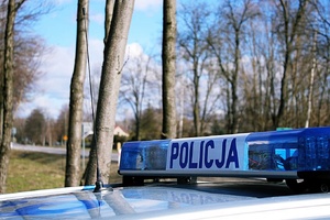 Napis POLICJA na radiowozie, w tle widać drogę.