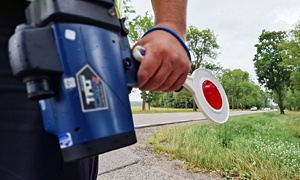 Policjant trzyma ręczny miernik prędkości i tarczkę do zatrzymywania pojazdów.