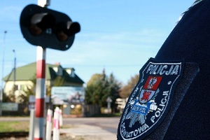 Policjant stoi przy przejeździe kolejowym.